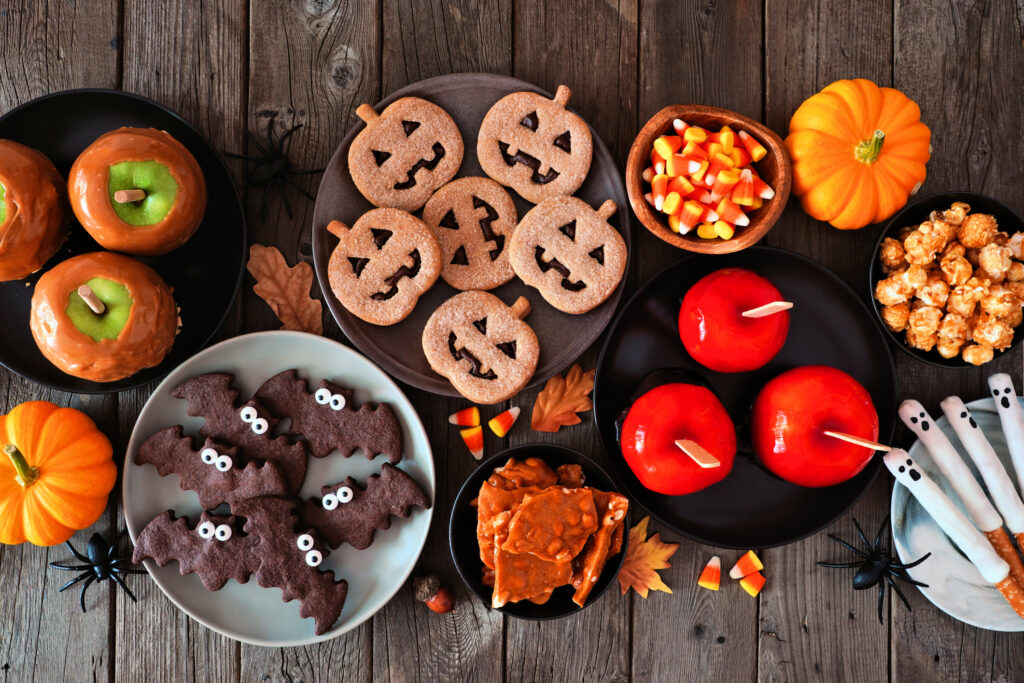 Rustic Halloween treat table scene over a dark wood background. Top view. Variety of candied apples, cookies, candy and sweets.