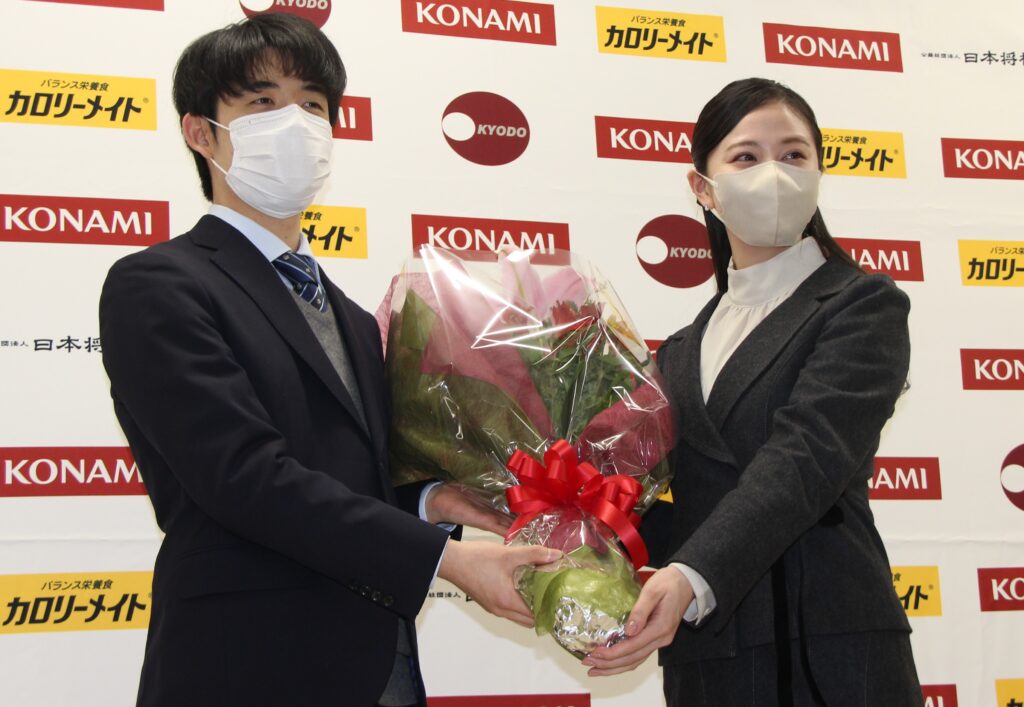 棋王戦を特別協賛するコナミグループの担当者から花束を贈られる藤井聡太竜王（左）