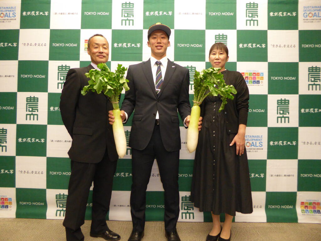 東農大の象徴、大根を手に持つ宮崎投手（中央）。左は父親の正浩さん、右は母親の奈津江さん。