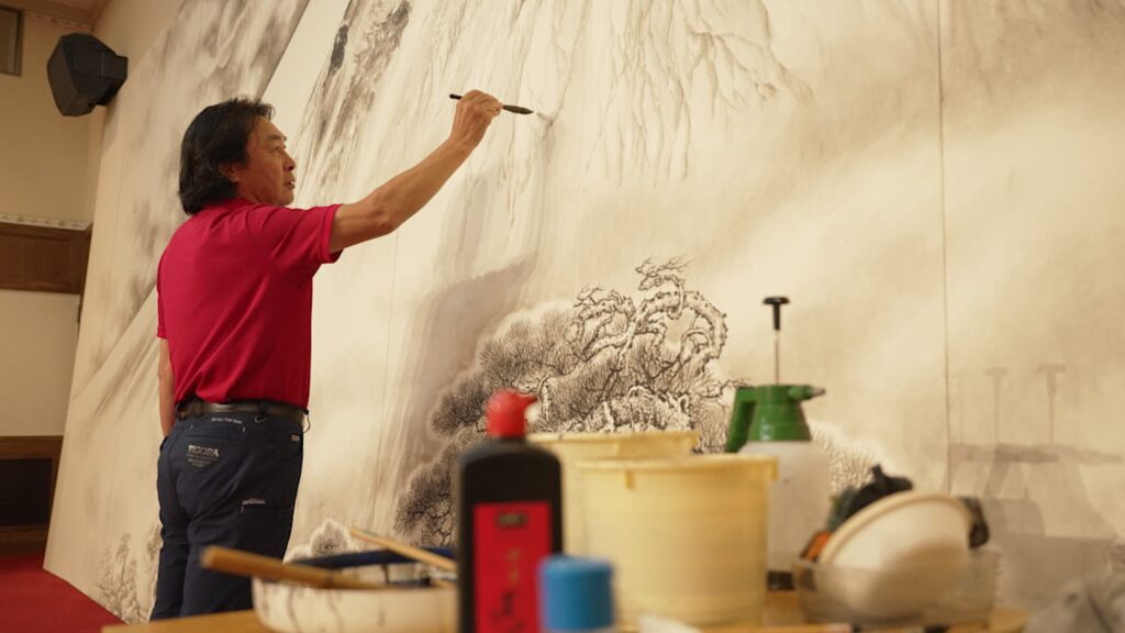 巨大水墨画の完成に向けて絵筆を走らせる曹さん＝長崎県西海市のアトリエ